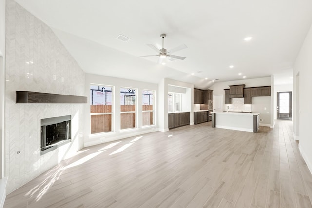 unfurnished living room featuring ceiling fan, lofted ceiling, a large fireplace, and light wood-type flooring