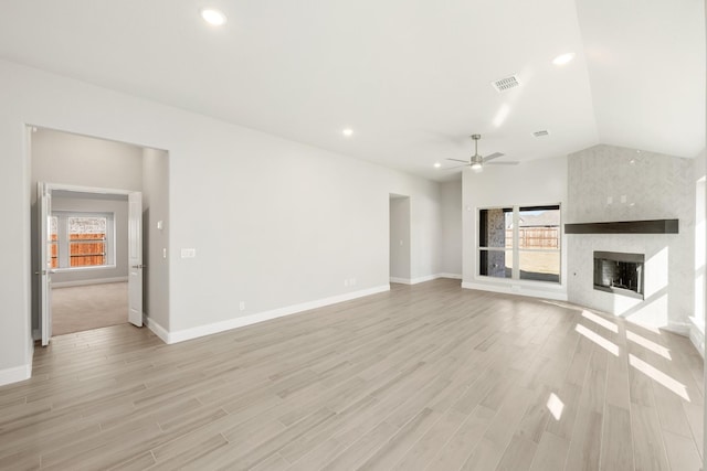 unfurnished living room featuring ceiling fan, a large fireplace, light hardwood / wood-style floors, and vaulted ceiling