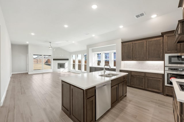 kitchen featuring lofted ceiling, sink, stainless steel appliances, a large fireplace, and a center island with sink