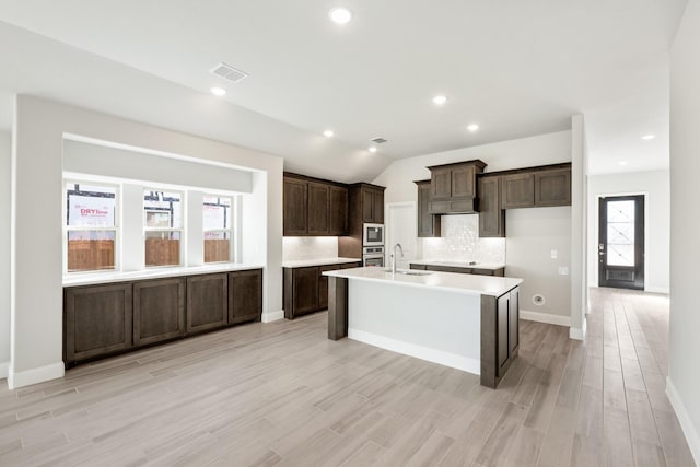 kitchen with vaulted ceiling, plenty of natural light, an island with sink, and backsplash