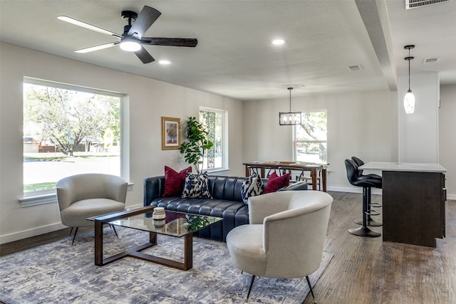 living room with ceiling fan with notable chandelier, hardwood / wood-style floors, and beamed ceiling