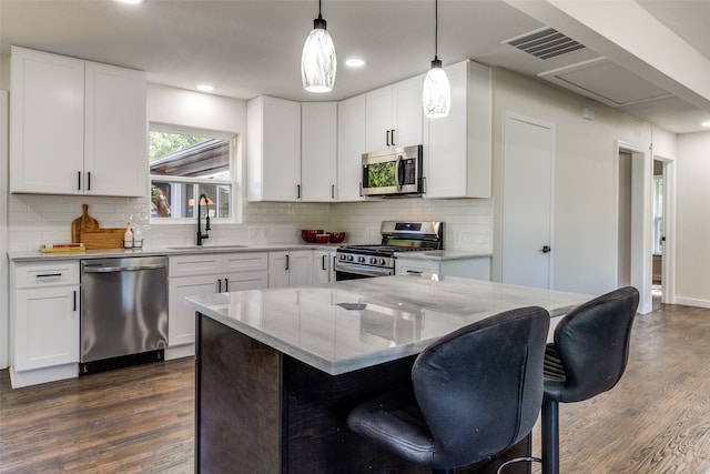 kitchen featuring appliances with stainless steel finishes, white cabinets, decorative light fixtures, and sink