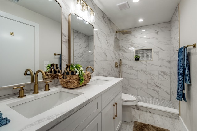 bathroom with toilet, a tile shower, and vanity