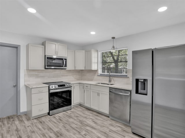 kitchen with white cabinetry, appliances with stainless steel finishes, hanging light fixtures, sink, and light hardwood / wood-style floors