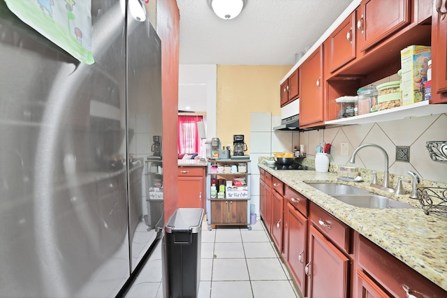 kitchen featuring tasteful backsplash, light stone counters, sink, and stainless steel refrigerator