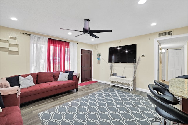 living room with hardwood / wood-style flooring, ceiling fan, and a textured ceiling