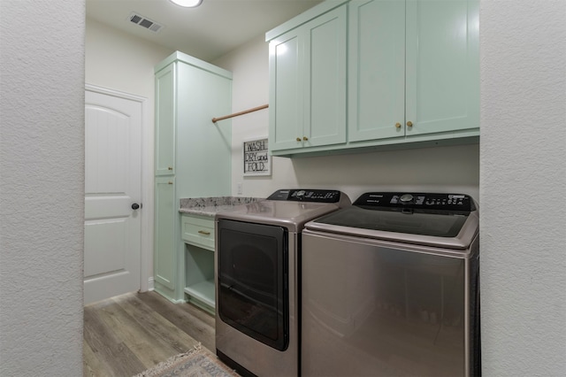 clothes washing area featuring cabinets, light hardwood / wood-style floors, and washer and dryer