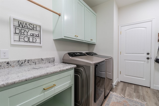 laundry room featuring washing machine and dryer, cabinets, and light hardwood / wood-style flooring