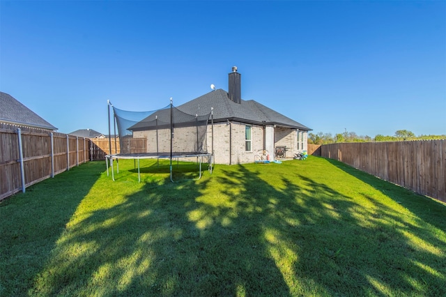 rear view of property featuring a trampoline and a lawn