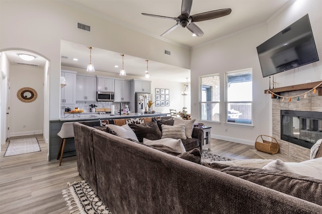 living room with light wood-type flooring, a fireplace, ceiling fan, and crown molding