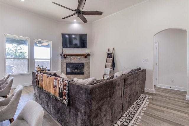 living room with ceiling fan, a stone fireplace, light hardwood / wood-style flooring, and crown molding