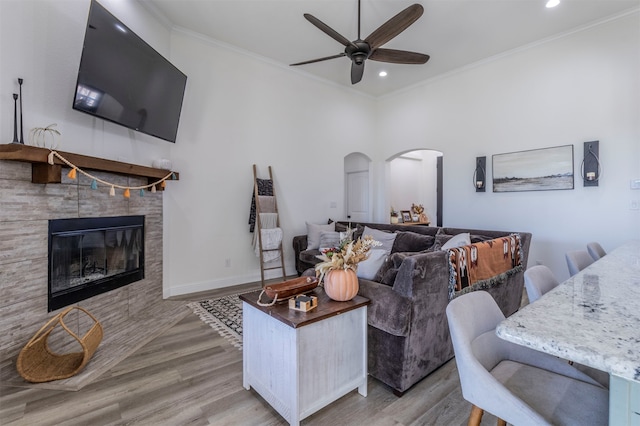 living room with ceiling fan, a tile fireplace, light hardwood / wood-style floors, and crown molding