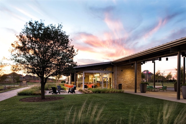 back house at dusk featuring a yard and a patio area