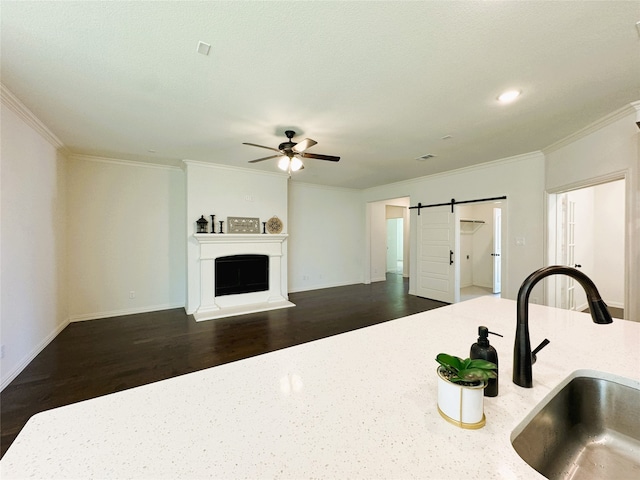 kitchen with a barn door, ceiling fan, crown molding, and dark hardwood / wood-style flooring