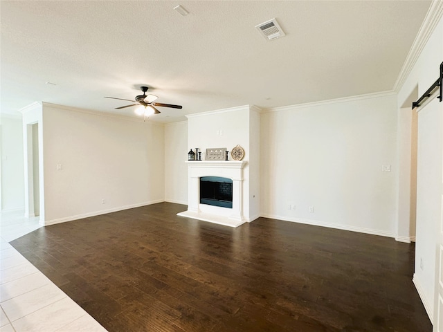 unfurnished living room with ornamental molding, dark wood-type flooring, a barn door, and ceiling fan