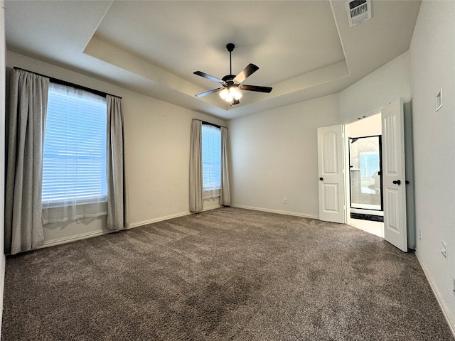 spare room with ceiling fan, plenty of natural light, a raised ceiling, and dark carpet