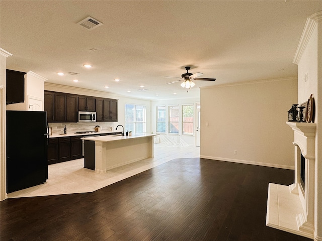 kitchen with ornamental molding, appliances with stainless steel finishes, an island with sink, ceiling fan, and light hardwood / wood-style flooring