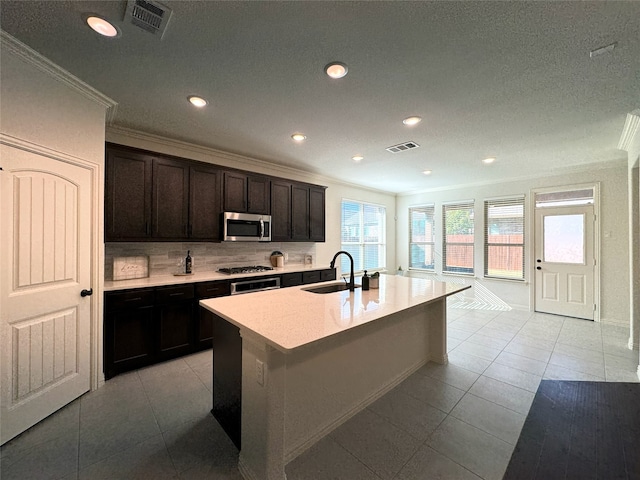 kitchen with stainless steel appliances, sink, crown molding, and an island with sink