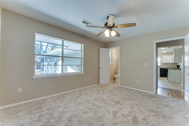 unfurnished bedroom featuring connected bathroom, light carpet, and ceiling fan