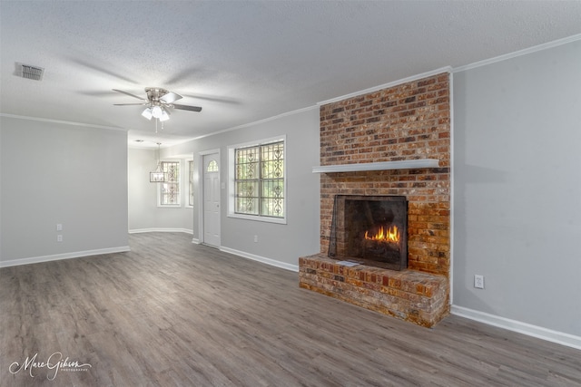 unfurnished living room with a brick fireplace, dark wood-type flooring, a textured ceiling, ornamental molding, and ceiling fan