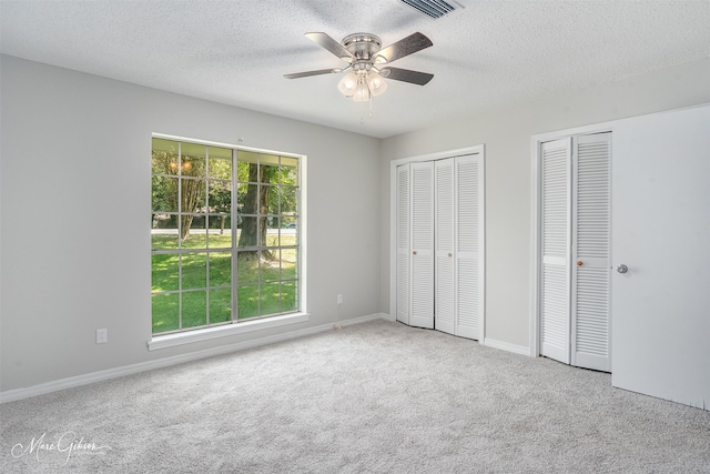 unfurnished bedroom featuring ceiling fan, a textured ceiling, two closets, and light colored carpet