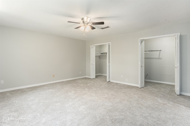 unfurnished bedroom featuring ceiling fan, a textured ceiling, two closets, and light colored carpet