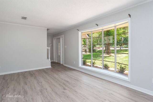 spare room featuring a textured ceiling, ornamental molding, and light hardwood / wood-style flooring