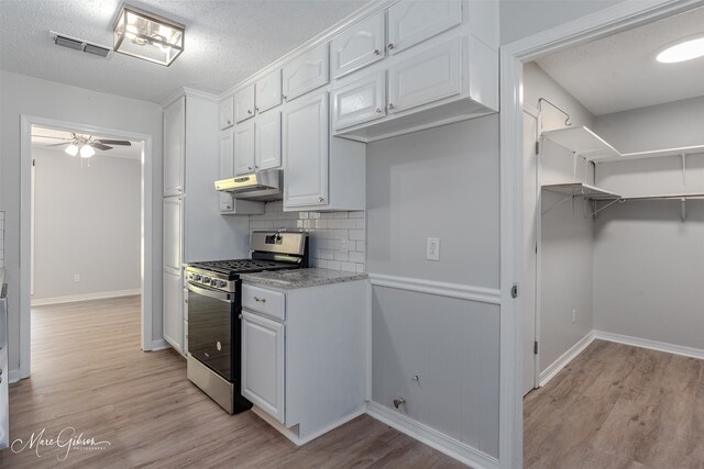 kitchen with stainless steel gas stove, white cabinetry, a textured ceiling, decorative backsplash, and light hardwood / wood-style flooring