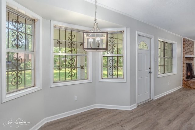 foyer with a fireplace, wood-type flooring, a chandelier, and crown molding