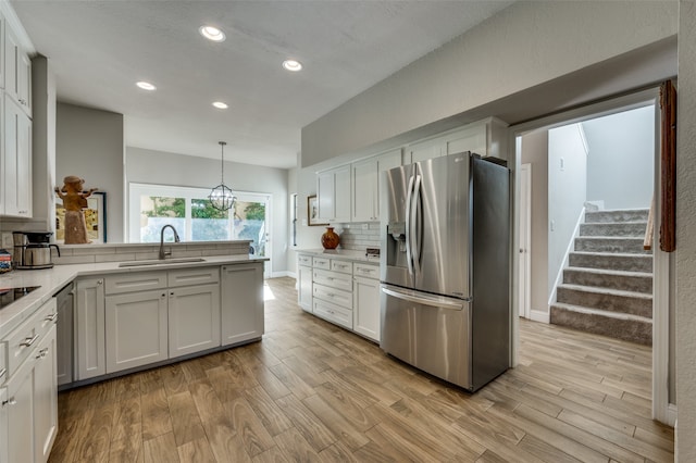 kitchen featuring white cabinetry, light wood-type flooring, decorative light fixtures, stainless steel fridge with ice dispenser, and sink