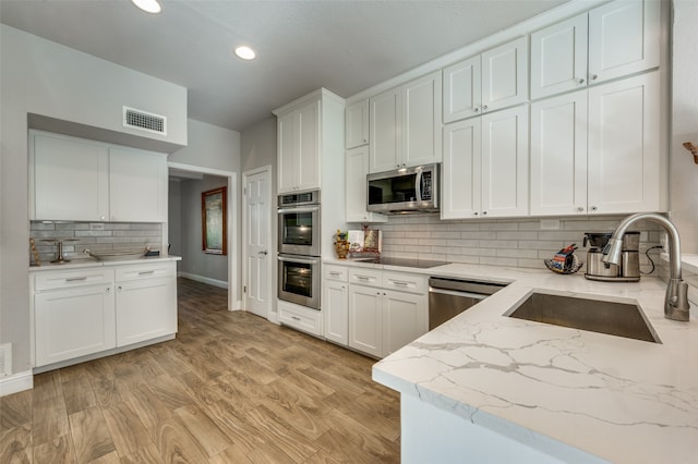 kitchen featuring tasteful backsplash, stainless steel appliances, light wood-type flooring, sink, and white cabinets