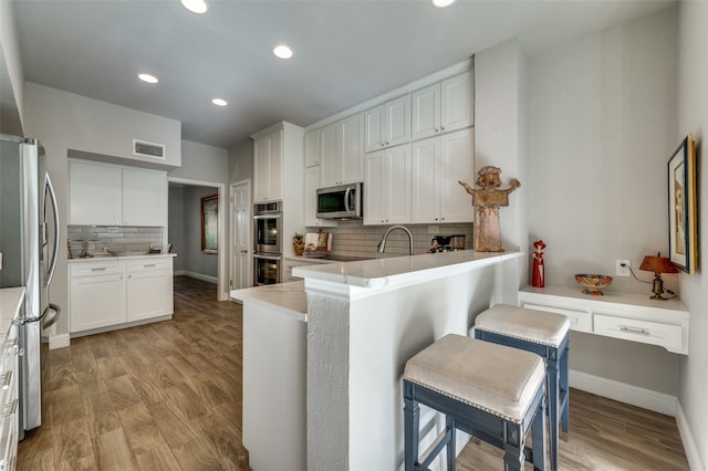 kitchen with backsplash, white cabinetry, appliances with stainless steel finishes, and a kitchen bar