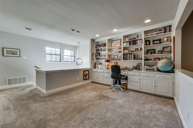 unfurnished office featuring a textured ceiling, light colored carpet, and built in desk