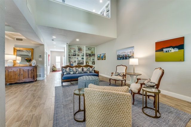 living room featuring a towering ceiling, built in features, and light wood-type flooring