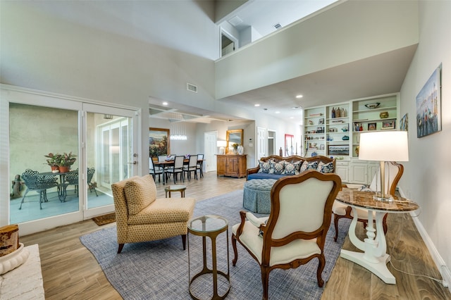 living room featuring built in shelves, light hardwood / wood-style floors, and a high ceiling