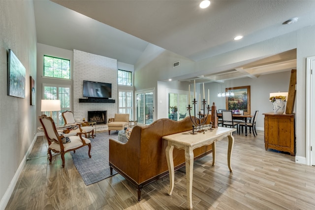 living room with a brick fireplace, light hardwood / wood-style flooring, vaulted ceiling with beams, and a chandelier