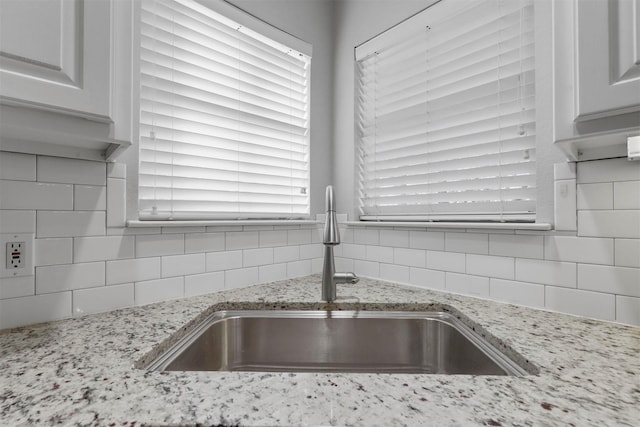 kitchen featuring tasteful backsplash, light stone countertops, sink, and white cabinets