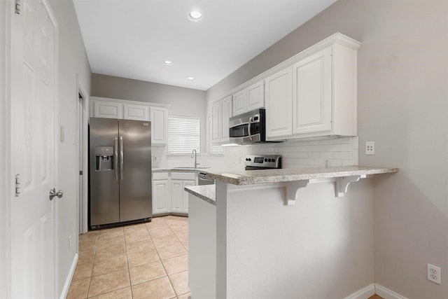 kitchen featuring white cabinets, appliances with stainless steel finishes, tasteful backsplash, a kitchen bar, and kitchen peninsula