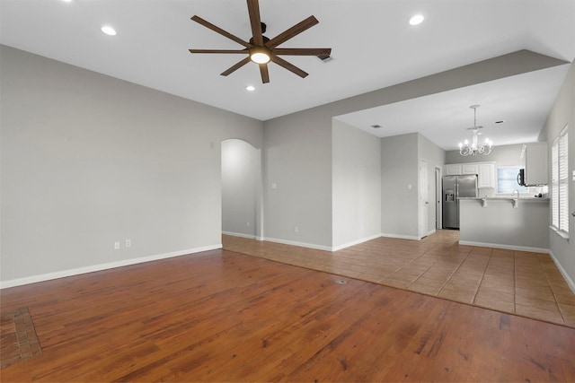 unfurnished living room featuring ceiling fan with notable chandelier and light wood-type flooring