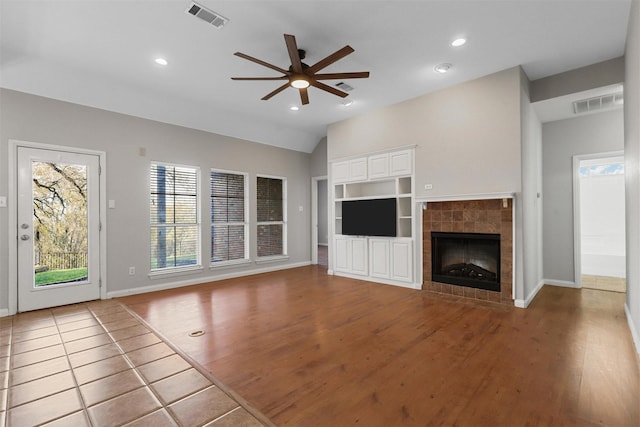 unfurnished living room with ceiling fan, a tile fireplace, built in features, hardwood / wood-style floors, and lofted ceiling