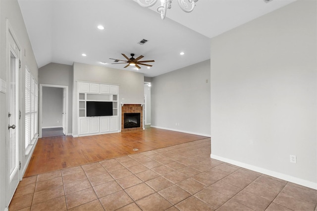 unfurnished living room featuring a tile fireplace, ceiling fan, light hardwood / wood-style floors, and vaulted ceiling