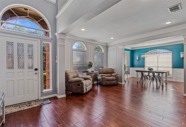 foyer entrance featuring ornate columns, crown molding, an inviting chandelier, a high ceiling, and dark hardwood / wood-style floors