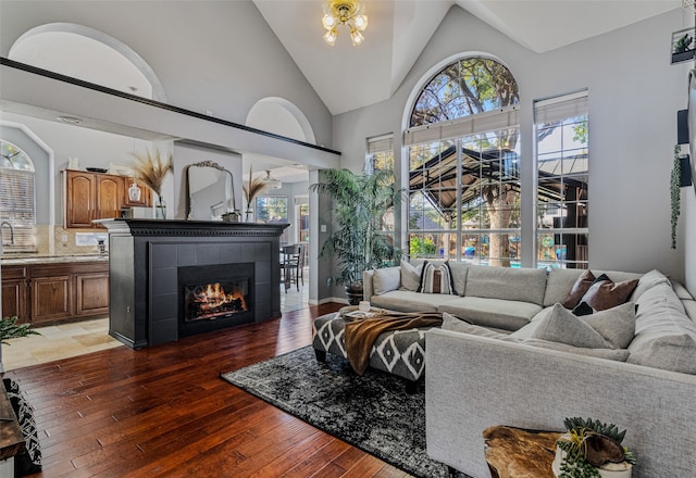 living room featuring dark wood-type flooring, high vaulted ceiling, and a tiled fireplace