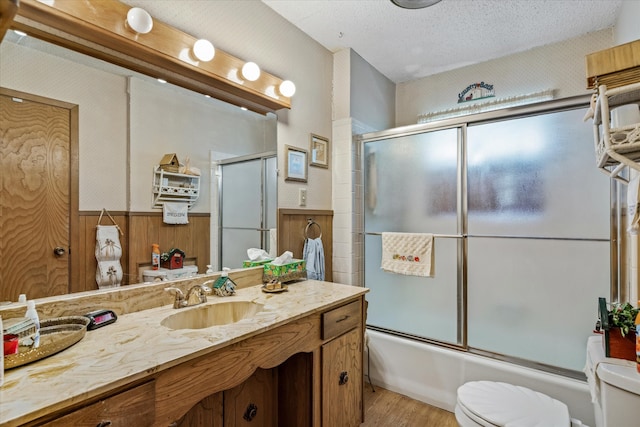 full bathroom with enclosed tub / shower combo, toilet, hardwood / wood-style flooring, a textured ceiling, and vanity