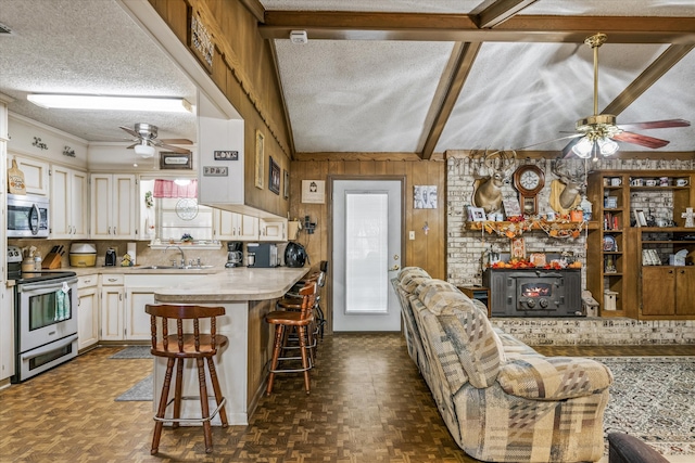 kitchen with wood walls, appliances with stainless steel finishes, a kitchen bar, a textured ceiling, and lofted ceiling with beams