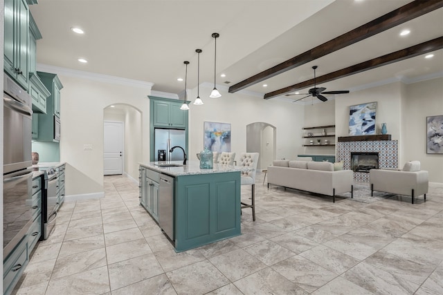 kitchen with beamed ceiling, sink, appliances with stainless steel finishes, decorative light fixtures, and an island with sink