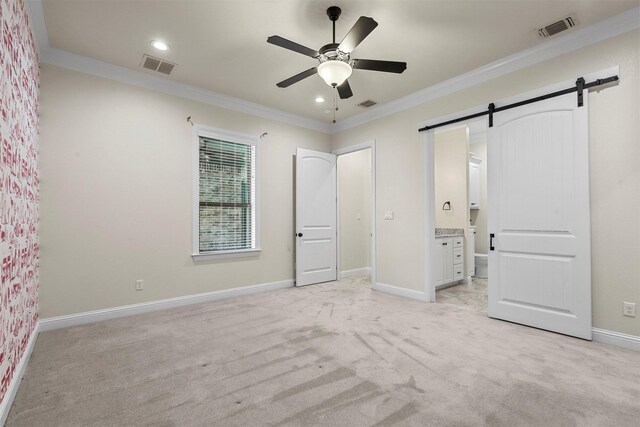 unfurnished bedroom with ornamental molding, ensuite bathroom, ceiling fan, a barn door, and light colored carpet