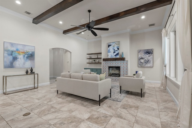 living room featuring a tiled fireplace, beamed ceiling, crown molding, and ceiling fan