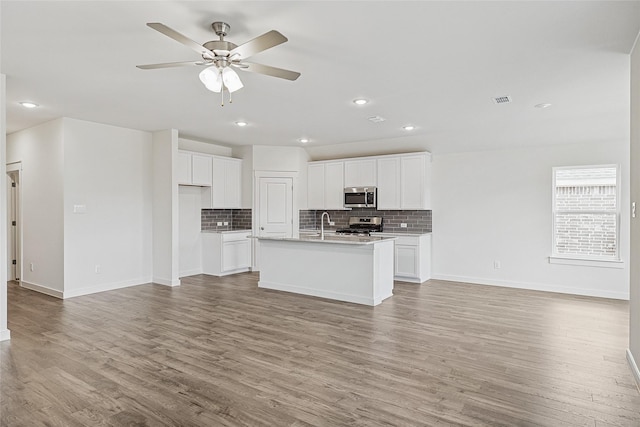 kitchen featuring light wood finished floors, appliances with stainless steel finishes, open floor plan, white cabinetry, and an island with sink