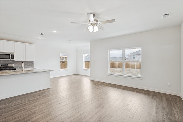 unfurnished living room with a ceiling fan, visible vents, baseboards, and wood finished floors